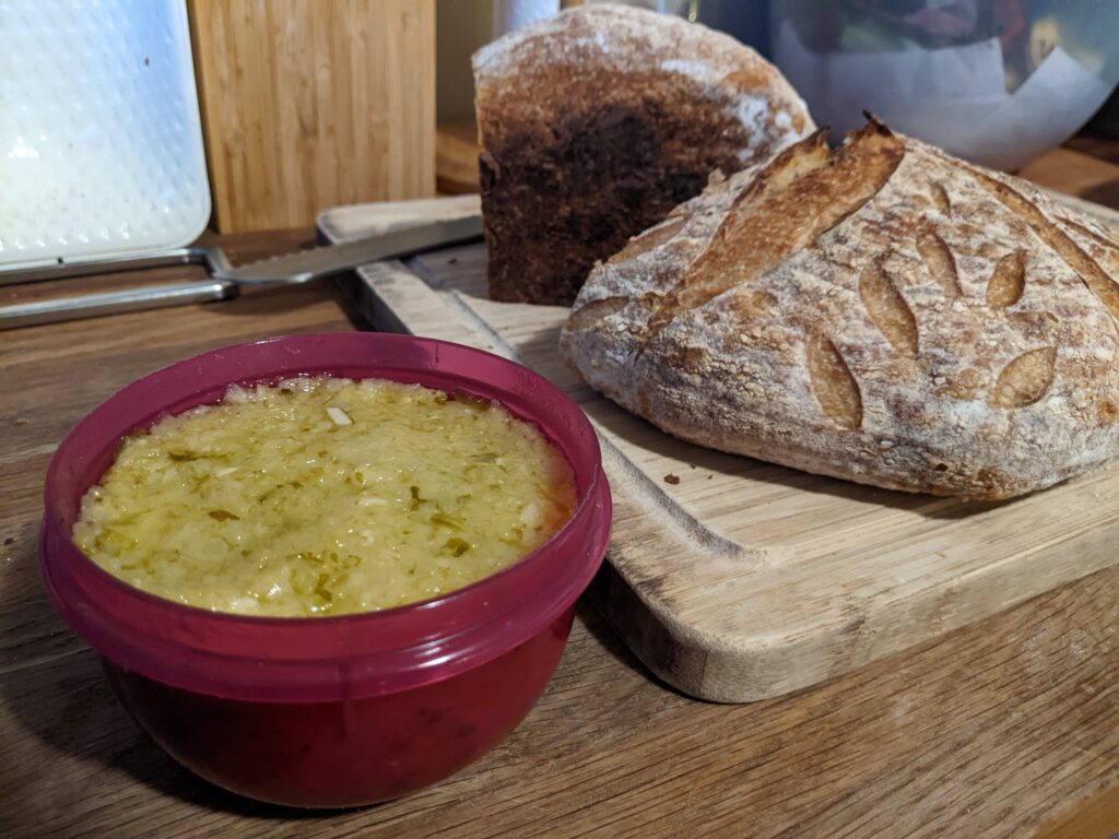 Ideal Lit'l bowl filled with stem pesto next to a wooden cutting board and a loaf of crusty bread.