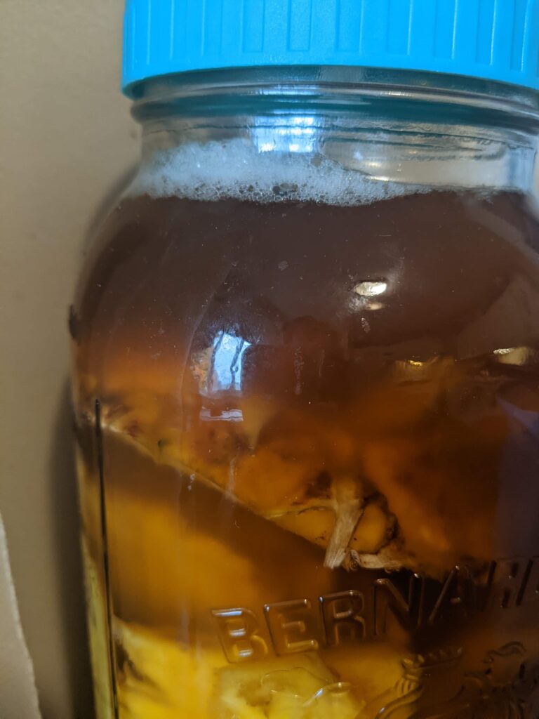 close up of the top of a mason jar with bubbles on the top of the brown liquid.