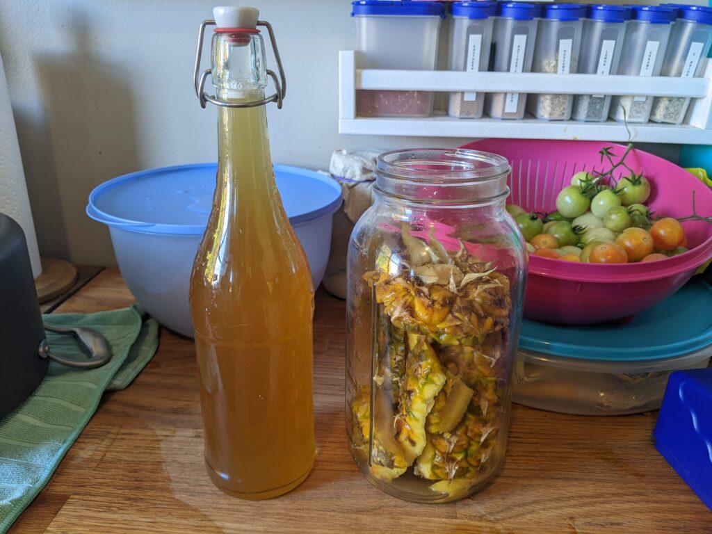 swingtop bottle of light brown liquid next to a 2L mason jar with pineapple rinds inside
