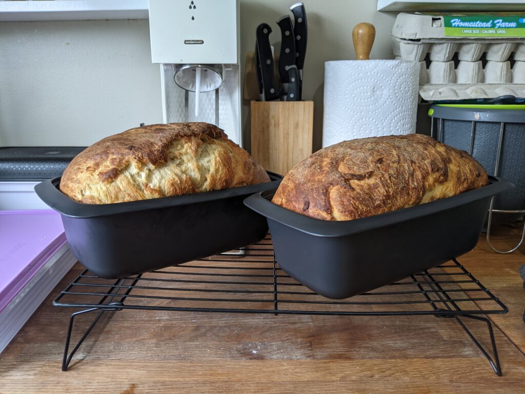 Two loaves of sandwich bread in Tupperware UltraPro loaf pans sitting on top of a cooling rack
